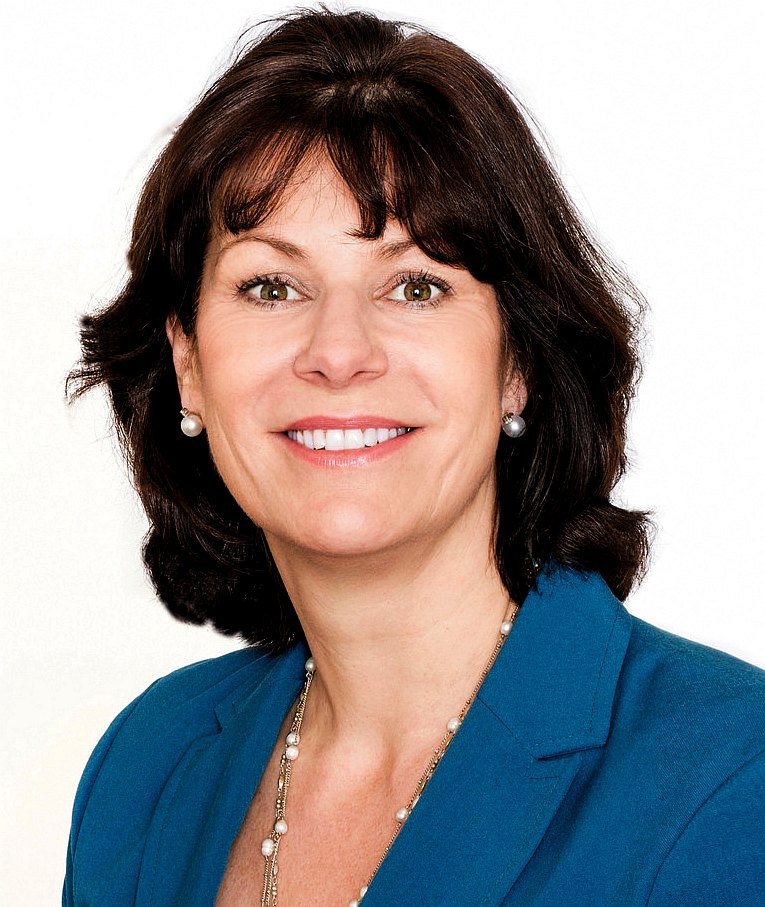 Claire Perry in blue outfit with pearl necklace and earrings